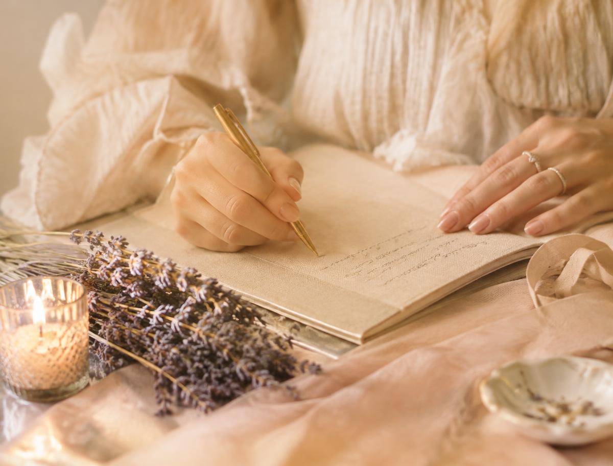 Hands writing in a journal beside lavender and a candle